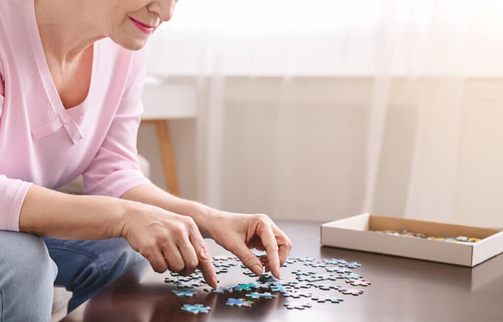 Senior woman playing jigsaw puzzle on wooden table at home